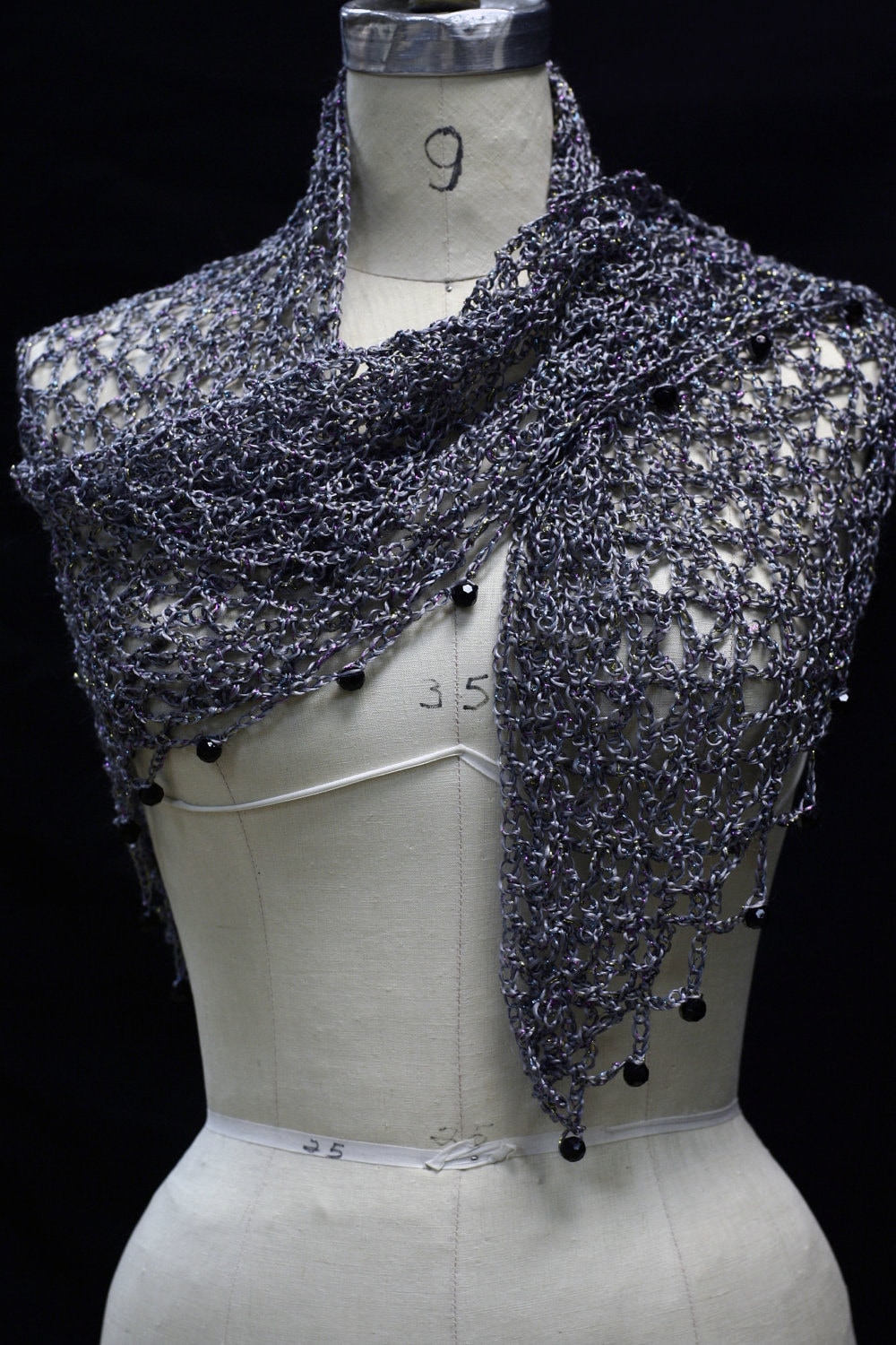 Grey beaded crochet shawl draped on a dress-form mannequin, front view with dark beads along the edge.